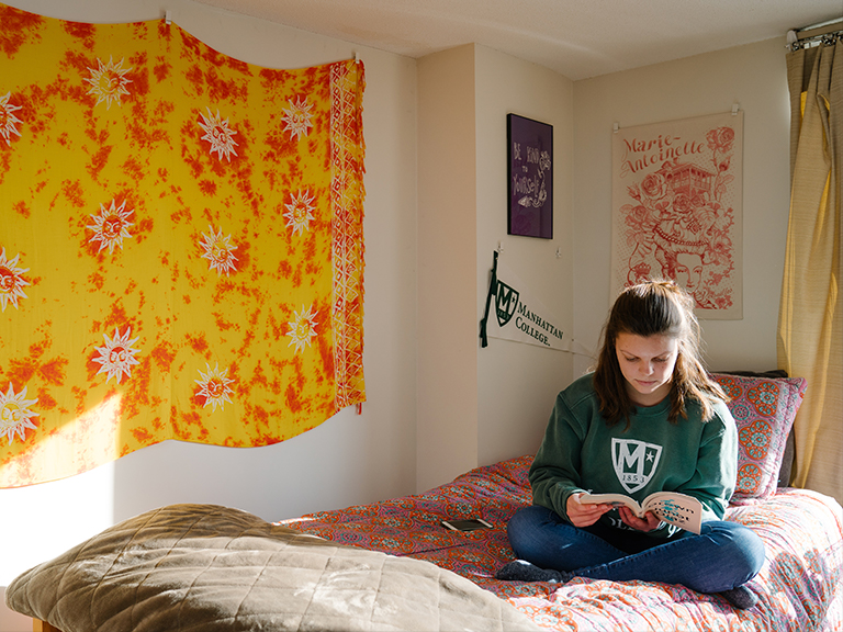 Female student on her bed reading in residence hall