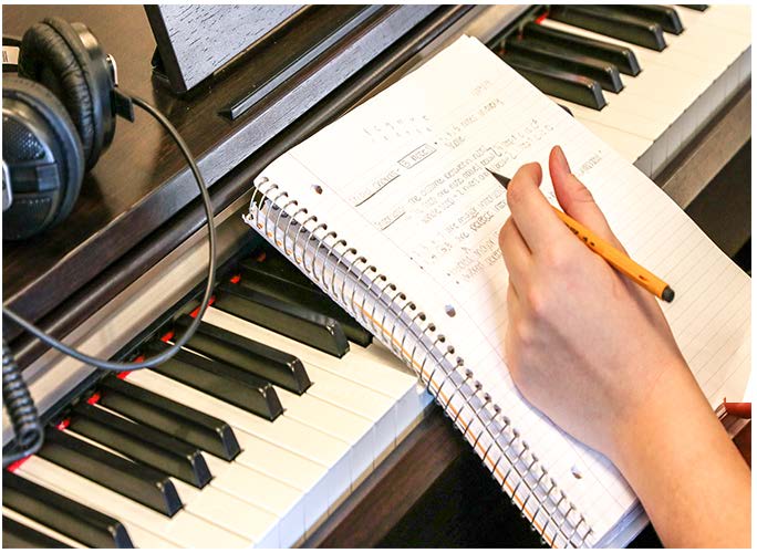Photograph of student hands holding a notebook and pen as it rests on keyboard