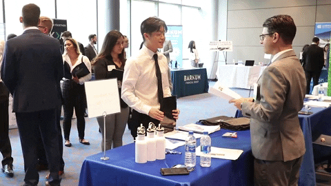 Male student dressed in a suit shaking hands with a recruiter at the Manhattan College career fair.