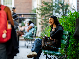 Manhattan University student smiling sitting on a bench talking to another student