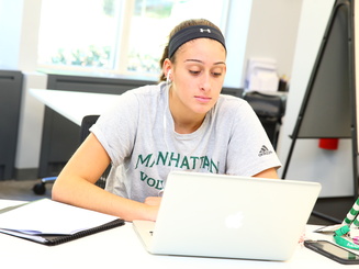 a student is seated at a table, working on a laptop computer