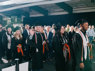 Graduate students process into the commencement ceremony at Manhattan University surrounded by family, faculty, and guests.