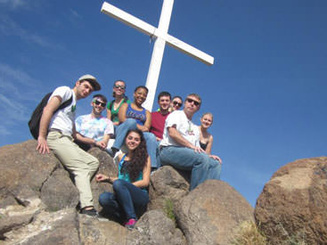 students gather on a rocky mountain top near a large white cross