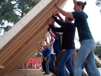 students help lift a wall to build a house