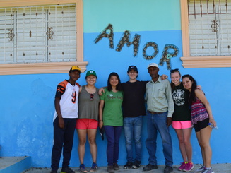 students stand and pose for a photo outside a school with the word "Amor" on the side