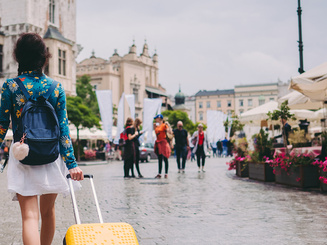 student walks through a foreign city with a rolling suitcase and a backpack