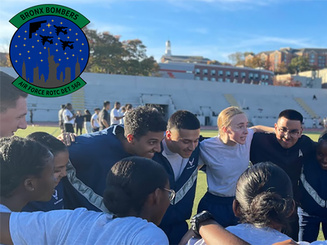 AFROTC cadets from Detachment 560 gather in a team huddle on a campus athletic field at Manhattan University, with the Bronx Bombers Air Force ROTC logo displayed in the upper left corner.