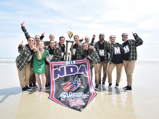 Jasper dancers at a beach holding a trophy and banner as national champions