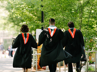 grads in regalia walk through campus