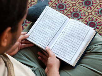 a student is seated on a rug, reading a book in Arabic