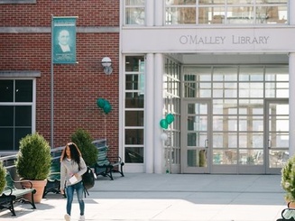 a student walks in front of the library building on campus