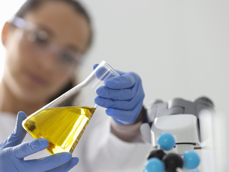 Manhattan University student looking at a beaker with yellow liquid in it