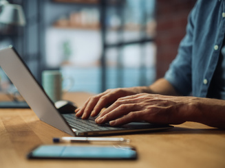 Close Up on Hands of a Male Specialist Working on Laptop Computer at Cozy Home Living Room while Sitting at a Table.
