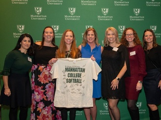 Manhattan University alumnae pose together at the Athletic Hall of Fame induction ceremony while holding a signed softball team shirt.