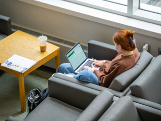 a student works on a laptop while seated in a chair near a window