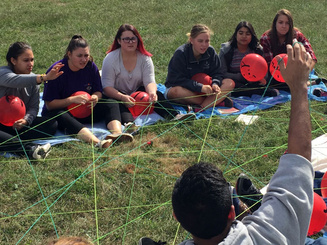 students sit in a circle with string and balloons as part of a group exercise