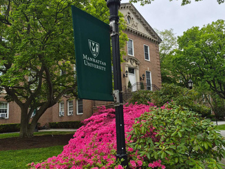 Manhattan University campus view with spring flowers and light pole with Manhattan University flag.