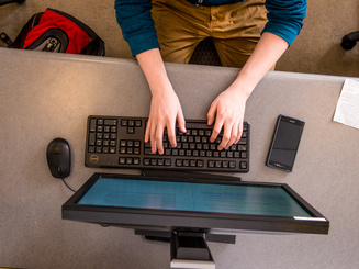 student's hands typing on computer keyboard from overhead view