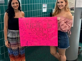 two women hold a promotional poster for the Women in STEM club
