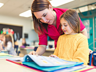 teacher helping student in classroom looking over their shoulder