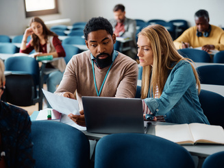 Education teacher assists a student with an assignment during class in classroom.