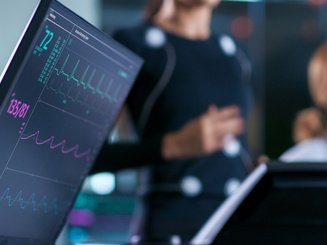 Monitor Showing EKG Reading of a Woman Athlete Running on a Treadmill in the Background, Two Specialists Supervise Exercise, Controlling Physical Activity. 