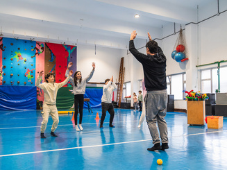 Students jumping and raising their arms, following their gym teacher's instructions during a physical education class