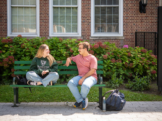 Manhattan University students sitting on a bench outside talking