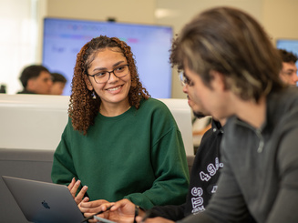 Manhattan University students in a classroom smiling and talking in front of a laptop