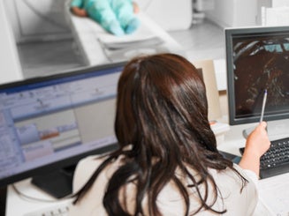 Back view a doctor sitting, working at computer, examining MRI results. Specialists wearing white robes