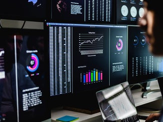 Stock market analysts monitoring real-time data, charts, and graphs on computer screens in a dark room.