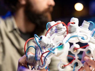 Focus on EEG headset used by IT professional in blurry background to communicate with artificial intelligence on computer.