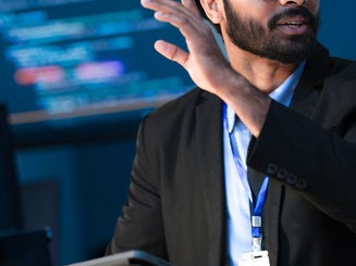 A data scientist holds a tablet in a command center.