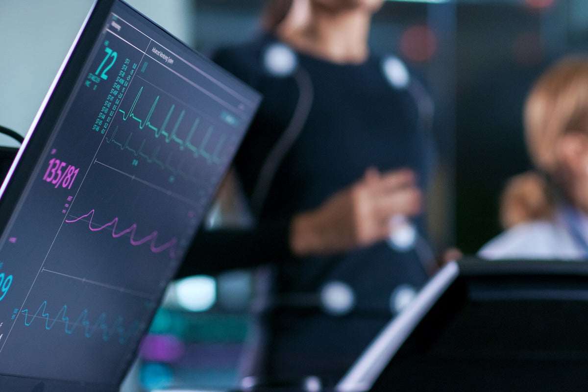 Monitor Showing EKG Reading of a Woman Athlete Running on a Treadmill in the Background, Two Specialists Supervise Exercise, Controlling Physical Activity. 