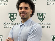 David Pozo, Manhattan University senior and Benjamin A. Gilman Scholarship recipient, standing with arms crossed in front of a Manhattan University backdrop.