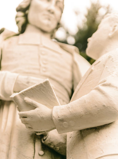 Statue of Saint John Baptist de La Salle teaching a student with an open book, representing the Lasallian mission of education.