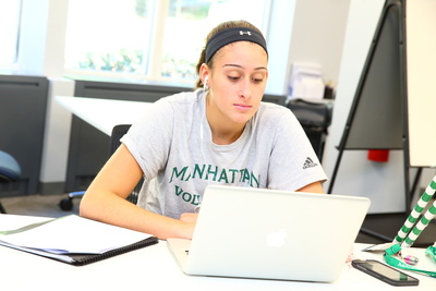 a student is seated at a table, working on a laptop computer