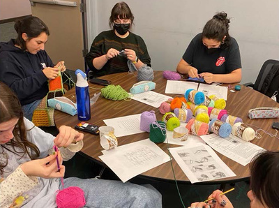 students sit around a table crocheting