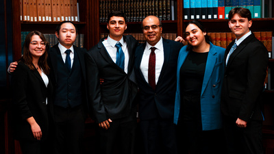 six people in suits pose for a photo in front of wall of bookshelves
