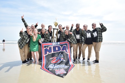 Jasper dancers at a beach holding a trophy and banner as national champions