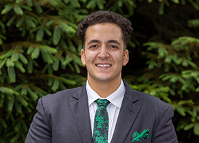 Portrait of Michael Troia, Admissions Counselor, smiling outdoors in a suit with a green tie.