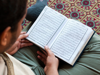 a student is seated on a rug, reading a book in Arabic