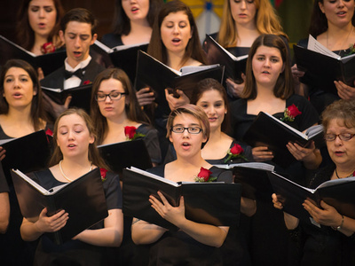 members of a choir hold music binders and sing at a concert