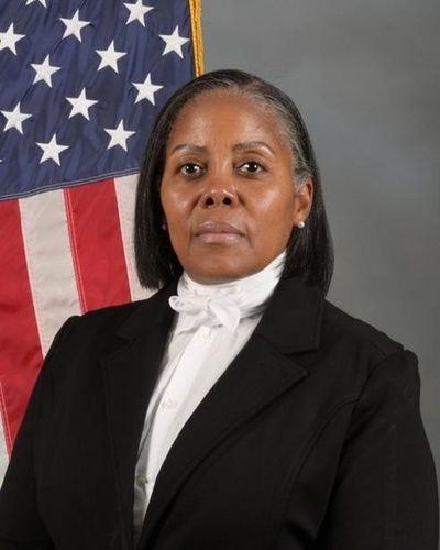 Official portrait of Dr. Rozela McCoy, Associate Professor of Aerospace Studies at AFROTC Detachment 560, posed in front of an American flag.