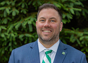 Portrait of Benjamin Boivin, Director of Undergraduate Admissions, smiling outdoors in a suit with a green striped tie.