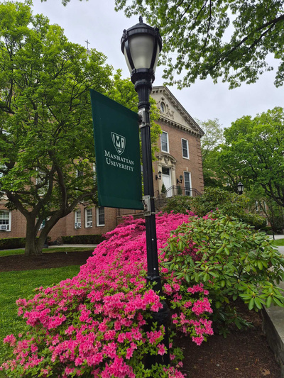 Manhattan University campus view with spring flowers and light pole with Manhattan University flag.
