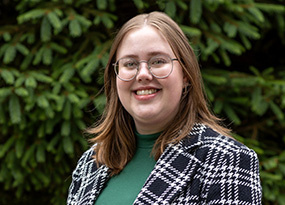 Portrait of Veronica Vaisman, Admissions Counselor, smiling outdoors wearing glasses and a patterned jacket.