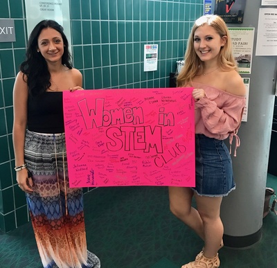 two women hold a promotional poster for the Women in STEM club