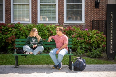 Manhattan University students sitting on a bench outside talking