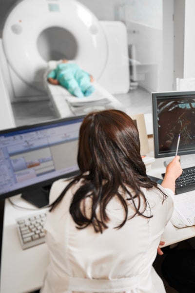 Back view a doctor sitting, working at computer, examining MRI results. Specialists wearing white robes